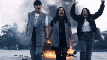 three women screaming in front of a burning vehicle