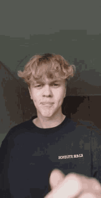 a young man with blonde hair is making a funny face while giving a thumbs up .