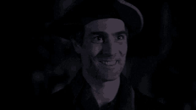 a man wearing a hat is smiling in a dark room