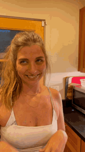 a woman in a white tank top smiles while standing in front of a microwave