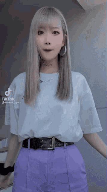a woman wearing purple pants and a white t-shirt has a tiktok sticker on her shirt