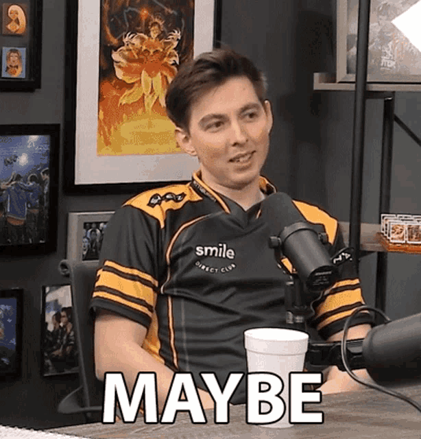 a man sitting in front of a microphone with the word maybe written on his shirt