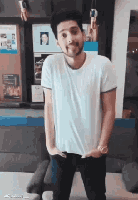 a man in a white shirt is standing in front of a couch with his hands in his pockets .