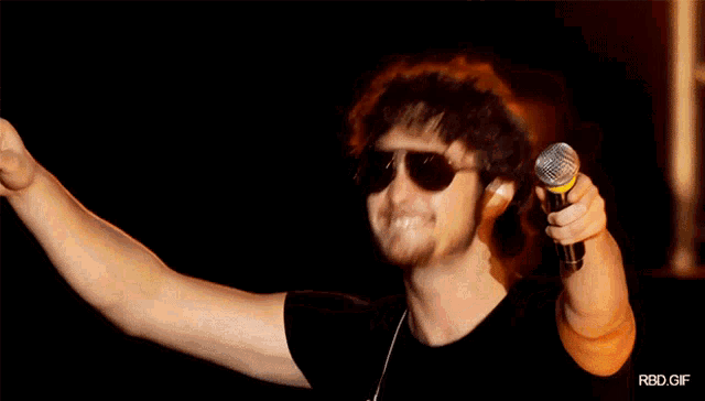 a man wearing sunglasses is singing into a microphone with rbd.gif below him