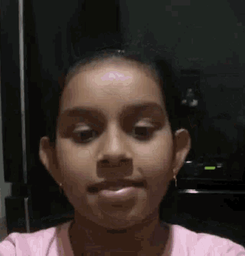 a young girl in a pink shirt is making a funny face and looking at the camera .