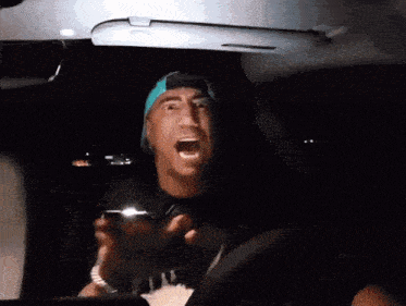 a man wearing a blue hat is driving a car and shouting
