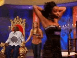 a woman in a black dress is standing in front of a man in a white shirt on a throne