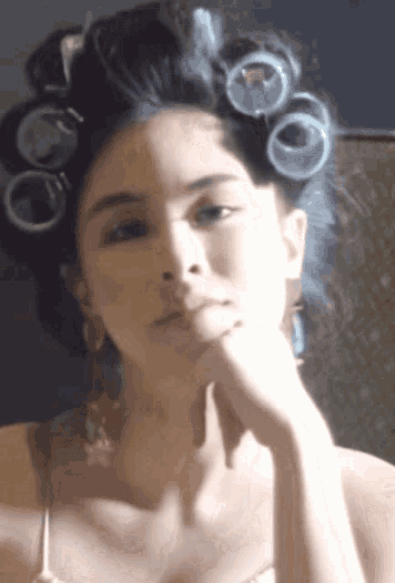 a woman with curlers in her hair looks at herself in a mirror