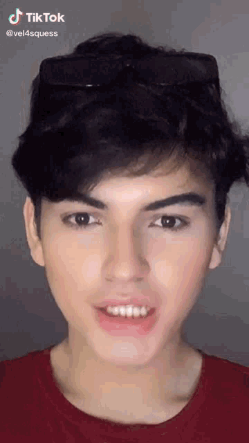 a young man wearing sunglasses and a red shirt is making a funny face