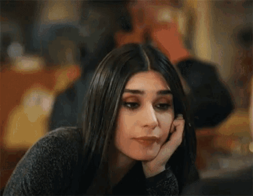 a woman is sitting at a table with her hand on her face and looking at the camera .