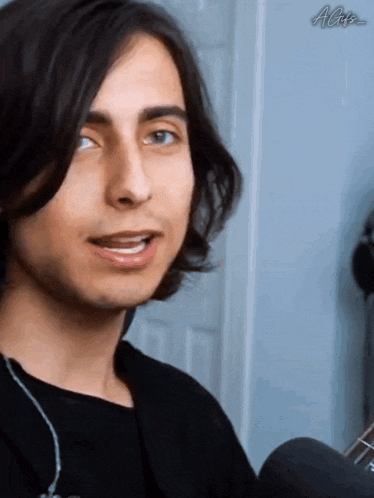 a young man with long hair is smiling and looking at the camera while wearing headphones .