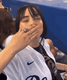 a woman is covering her mouth with her hand in a baseball stadium .