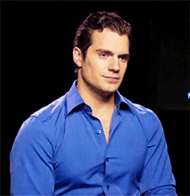 a man in a blue shirt is sitting in front of a black screen