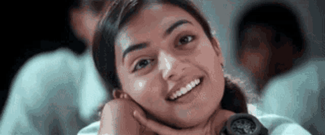 a young girl is smiling with her hand on her chin .