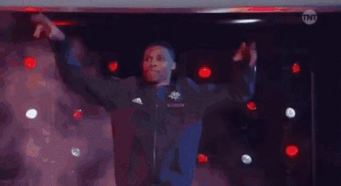 a man in a black jacket is standing on a stage with his arms outstretched in the air .