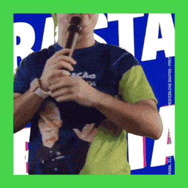 a man in a blue and yellow shirt holds a microphone in front of a sign that says rasta