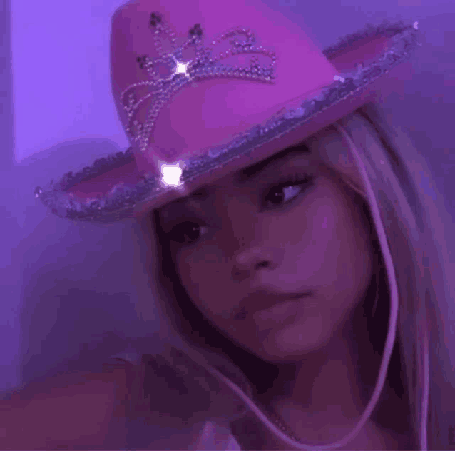 a woman wearing a pink cowboy hat with a tiara on it .
