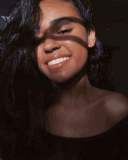 a woman with long dark hair is smiling with the sun shining on her face