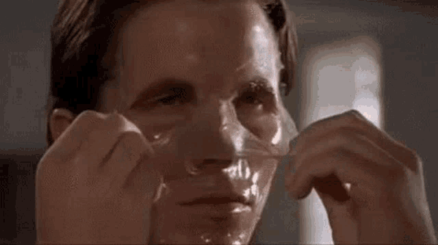 a close up of a man peeling off a mask from his face .