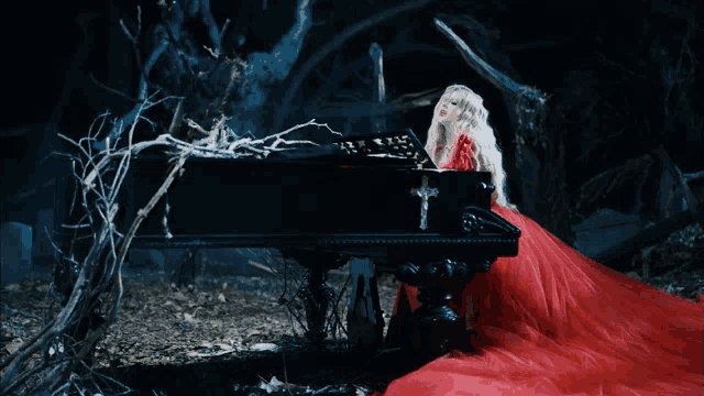a woman in a red dress is sitting at a piano with a cross on it