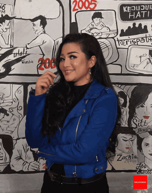 a woman in a blue jacket stands in front of a wall with drawings of people and the year 2005