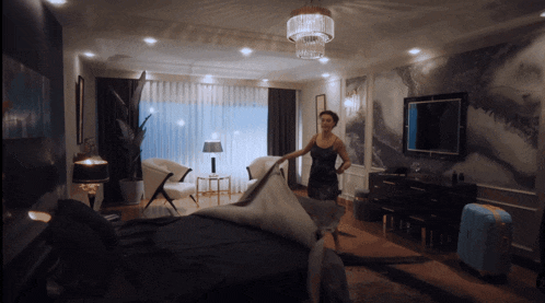 a woman is standing in a bedroom with a suitcase in front of her