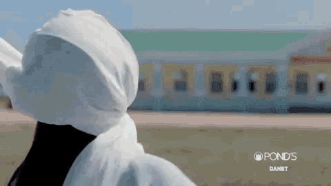 a woman wearing a white head scarf is standing in front of a pond 's ad