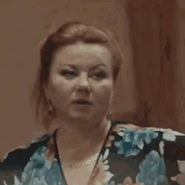 a woman wearing a floral shirt and a necklace is making a funny face .
