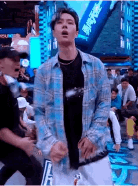 a man in a plaid shirt is dancing in front of a crowd .