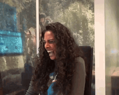 a woman with curly hair is sitting in front of a wall with a picture of a horse on it