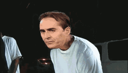 a man in a blue shirt is making a funny face in a dark room .