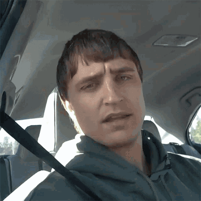 a man wearing a green hoodie is sitting in a car and making a funny face