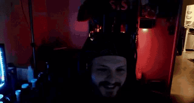 a man with a beard is wearing a black hat and headphones while sitting in front of a computer screen .