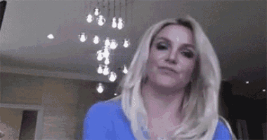 a woman in a blue shirt is standing in a living room with a chandelier in the background .