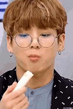a young man wearing glasses and earrings is eating a piece of cheese .