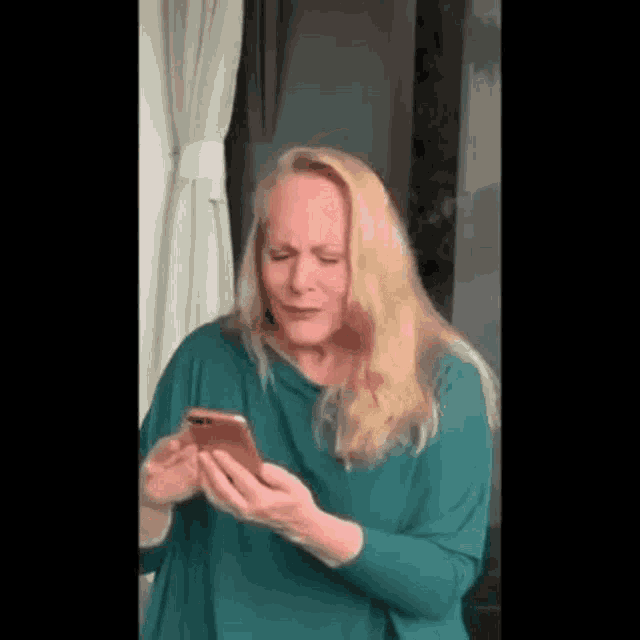 a woman in a green shirt is holding a cell phone in her hands .