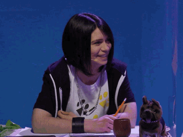 a woman sits at a table with a dog and a pencil in her hand