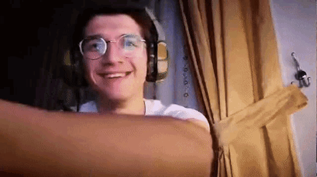 a young man wearing glasses and headphones is smiling while standing in front of a window .