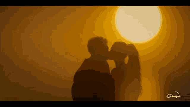 a silhouette of a man and woman kissing in front of a large sun .