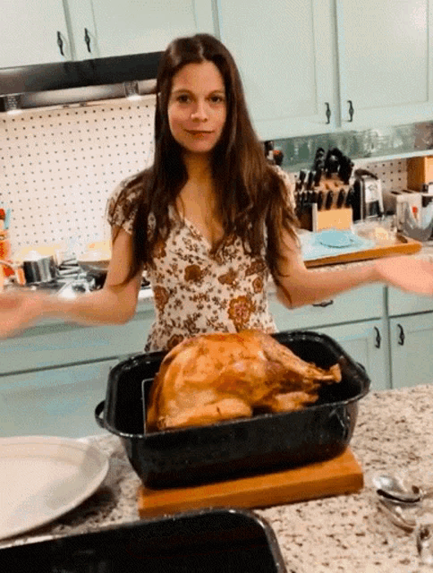 a woman is standing in front of a roasted turkey in a pan
