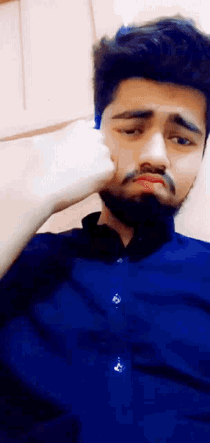 a man with a beard wearing a blue shirt is making a face