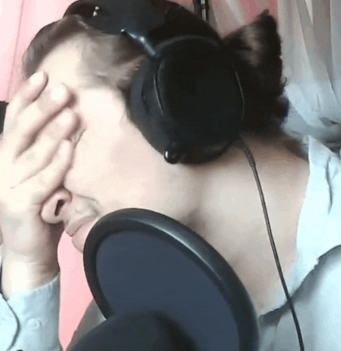 a person wearing headphones covering their face with their hand in front of a microphone
