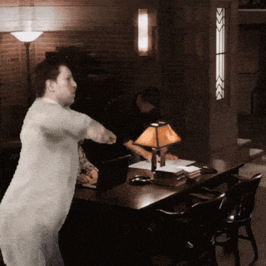 a man in a white shirt stands in front of a table with a lamp on it