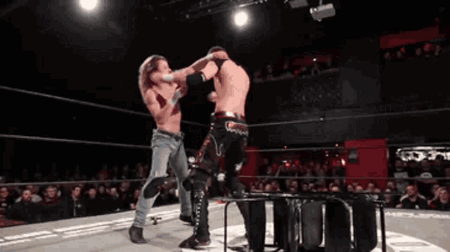 two men are wrestling in a ring with a crowd in the stands watching