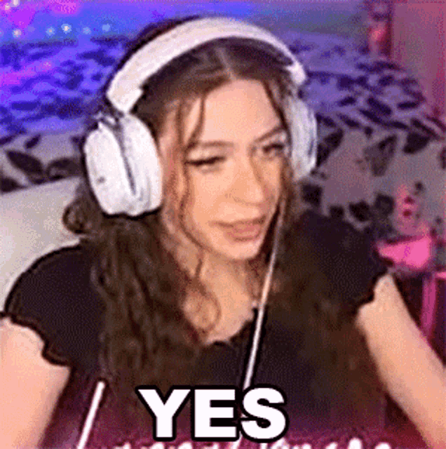 a woman wearing headphones and a black shirt is sitting in front of a computer and saying yes .