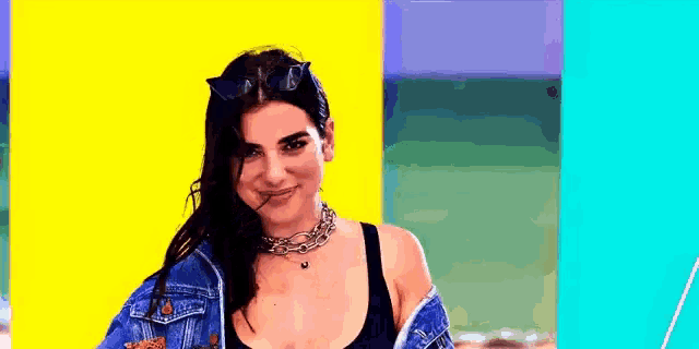 a woman wearing a denim jacket and sunglasses is standing in front of a colorful background .