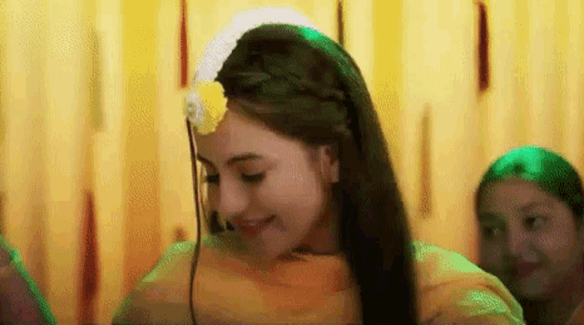 a woman wearing a yellow dress and a flower in her hair is smiling .