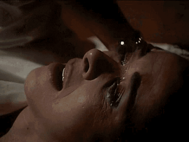 a man is laying on a bed in a dark room with two lamps on the side of the bed .
