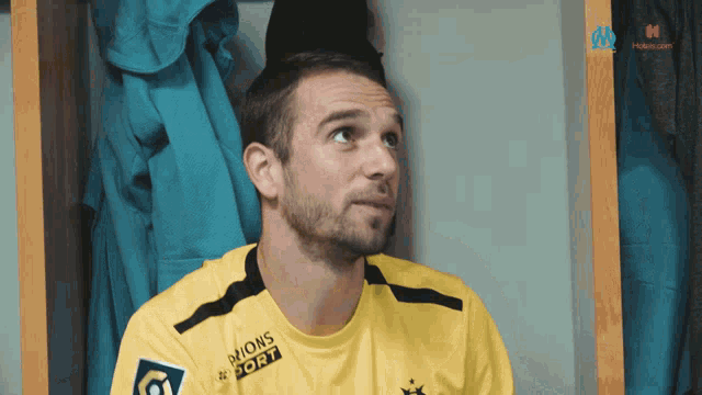 a man wearing a yellow jersey with the word sport on it is sitting in a locker room