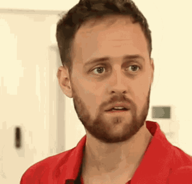 a man with a beard is wearing a red shirt and making a surprised face .
